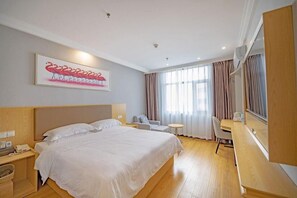 Habitación de hotel con una cama grande, un escritorio, una silla y un ventanal con cortinas.