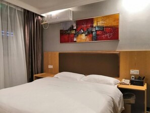 Una habitación de hotel con cama, mesita de noche, equipo de aire acondicionado y una obra de arte colgada en la pared.