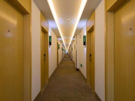A hotel hallway with wooden doors, green directional signs, and a carpeted floor.