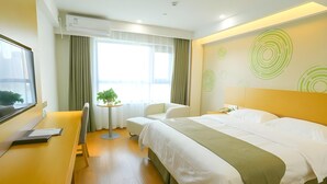 A modern hotel room with a bed, a desk, a chair, a small table with a plant, and a large window. - Greentree Inn Shangqiu Suiyang Avenue Hotel (Shangqiu)