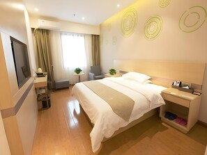 Camera d'albergo moderna con un letto grande, una scrivania, una sedia, una TV e un tavolino con una pianta.