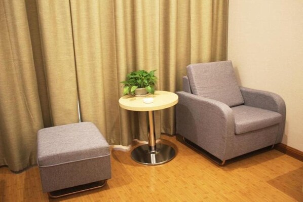 A room with a grey armchair, a small round table with a plant, and a matching ottoman. - Greentree Inn Zhengzhou Fangte Green Expo Park Shangdu Road (Zhengzhou)