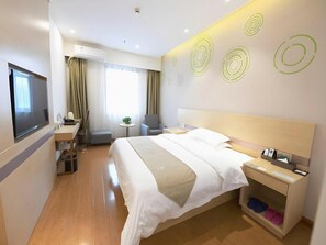 Una camera d'hotel con un letto, comodino, televisione, scrivania, sedia e un piccolo tavolino con una pianta.