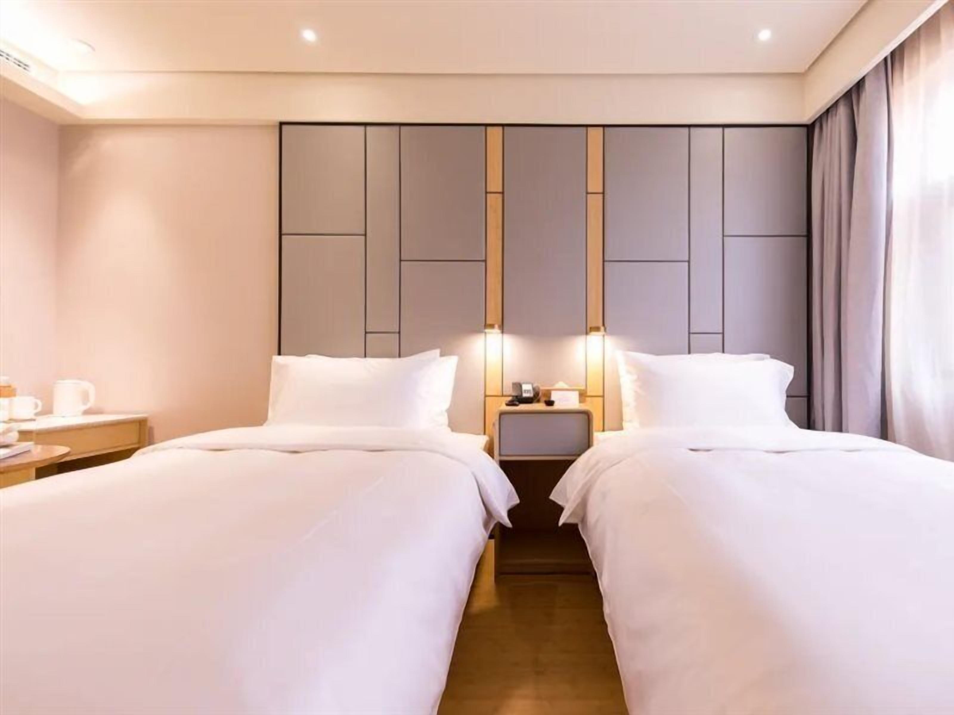 A hotel room with two beds, a nightstand with a lamp, and a wall panel design.