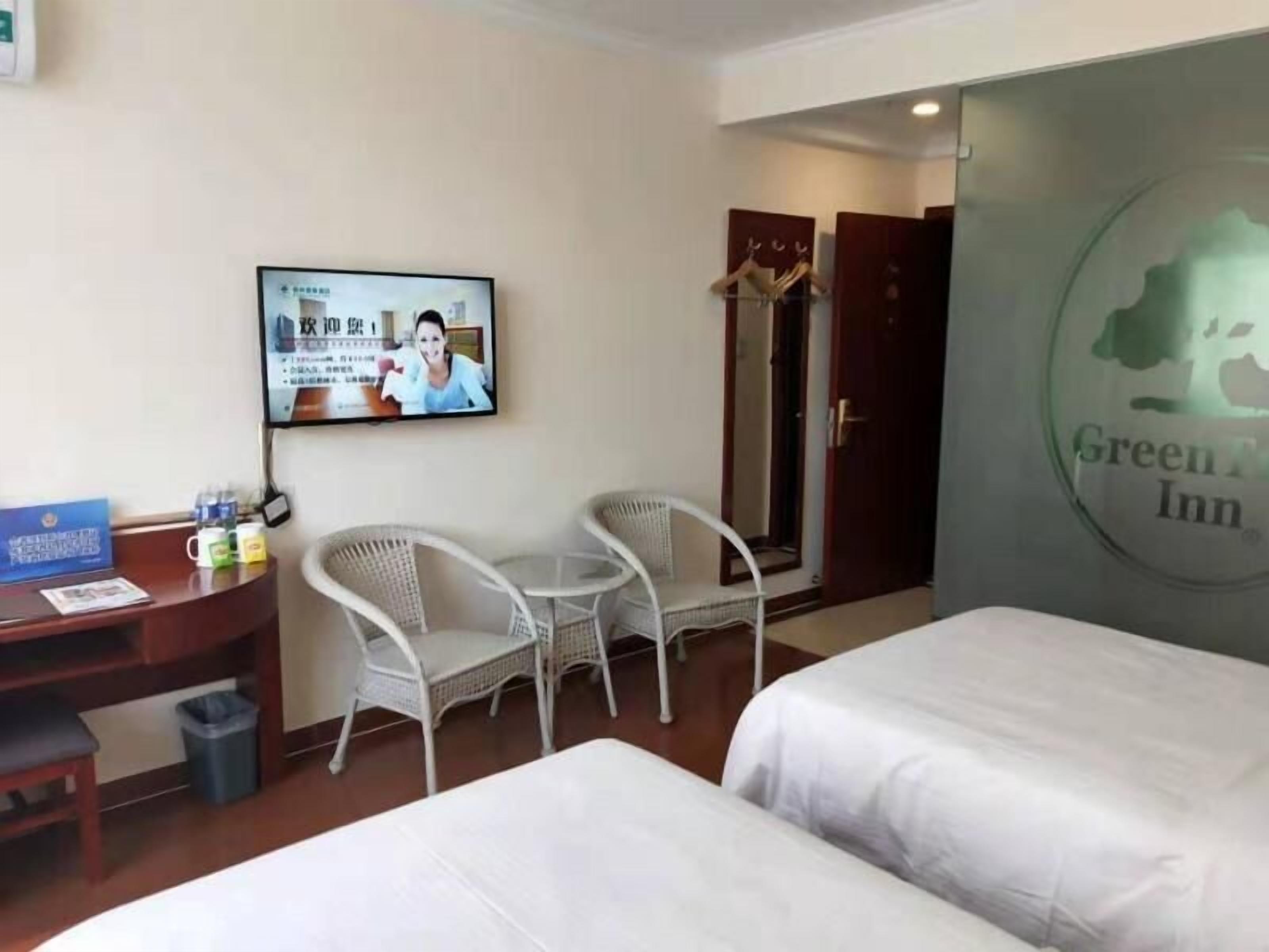 A hotel room with a bed, two white chairs, a desk with a computer monitor, and a television.