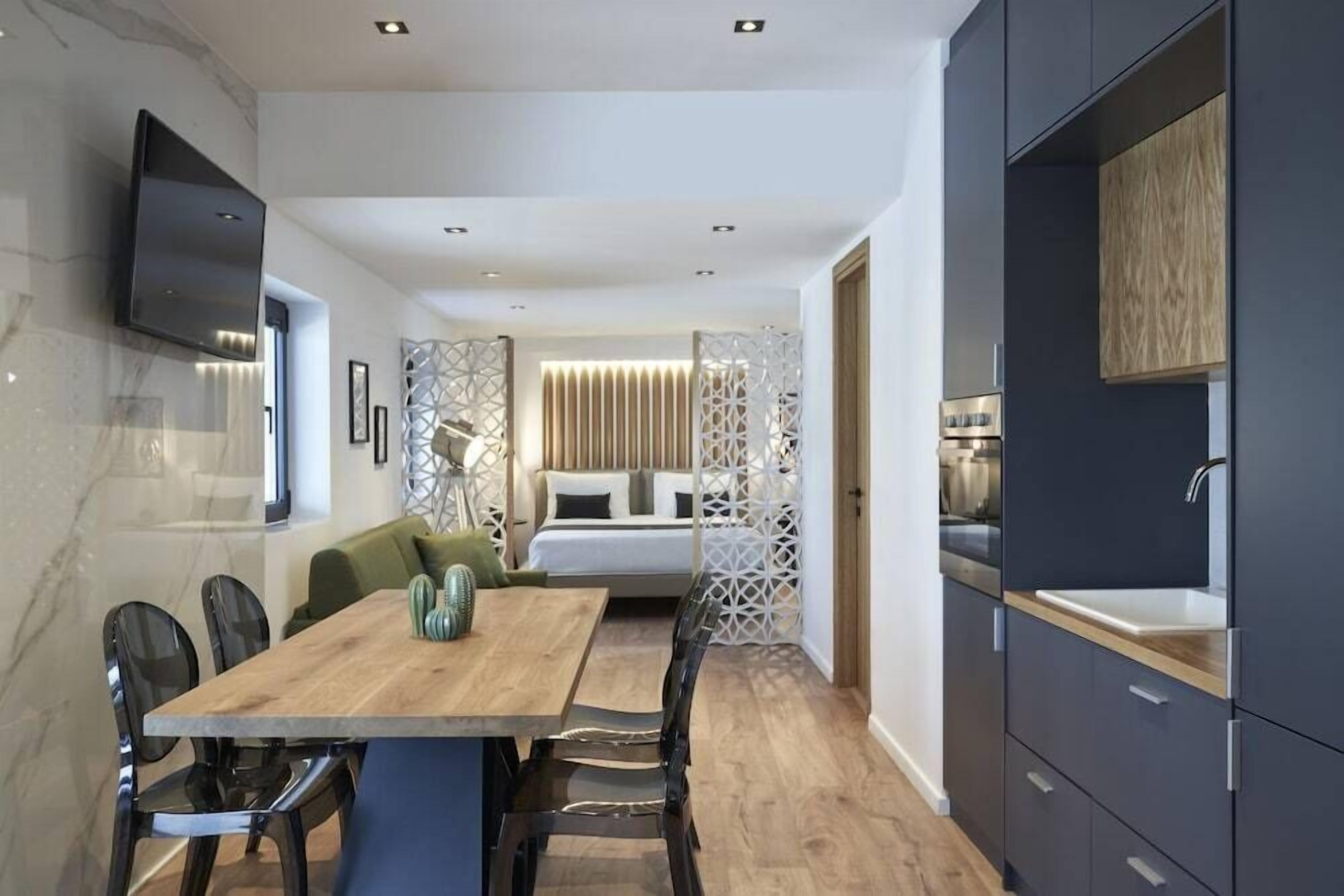 Una habitación de hotel moderna con una mesa de comedor de madera, sillas negras, un sofá, una cama y una cocina integrada.