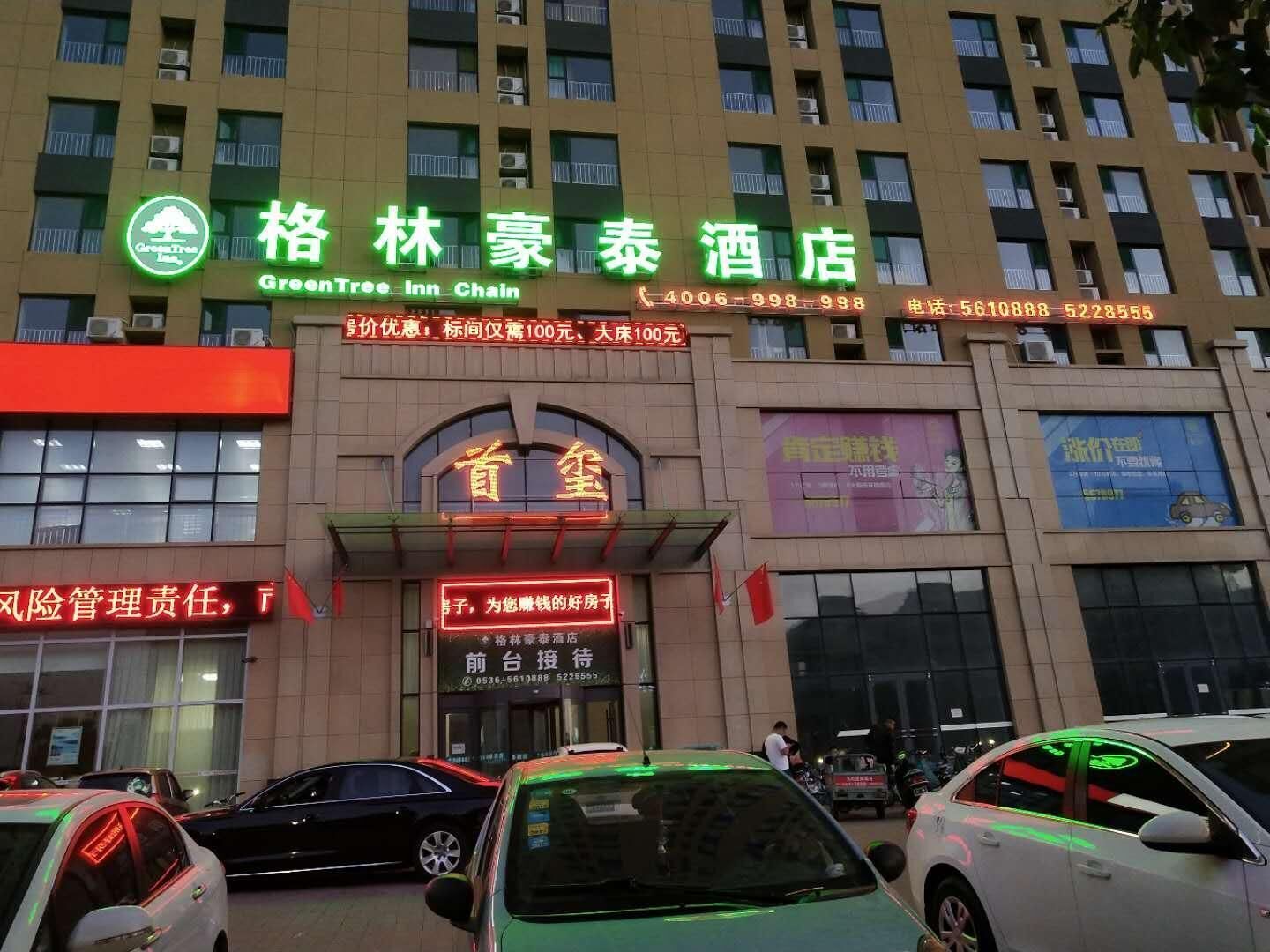 Un hotel con un llamativo letrero de la cadena GreenTree Inn, varios números de contacto y una entrada visible.