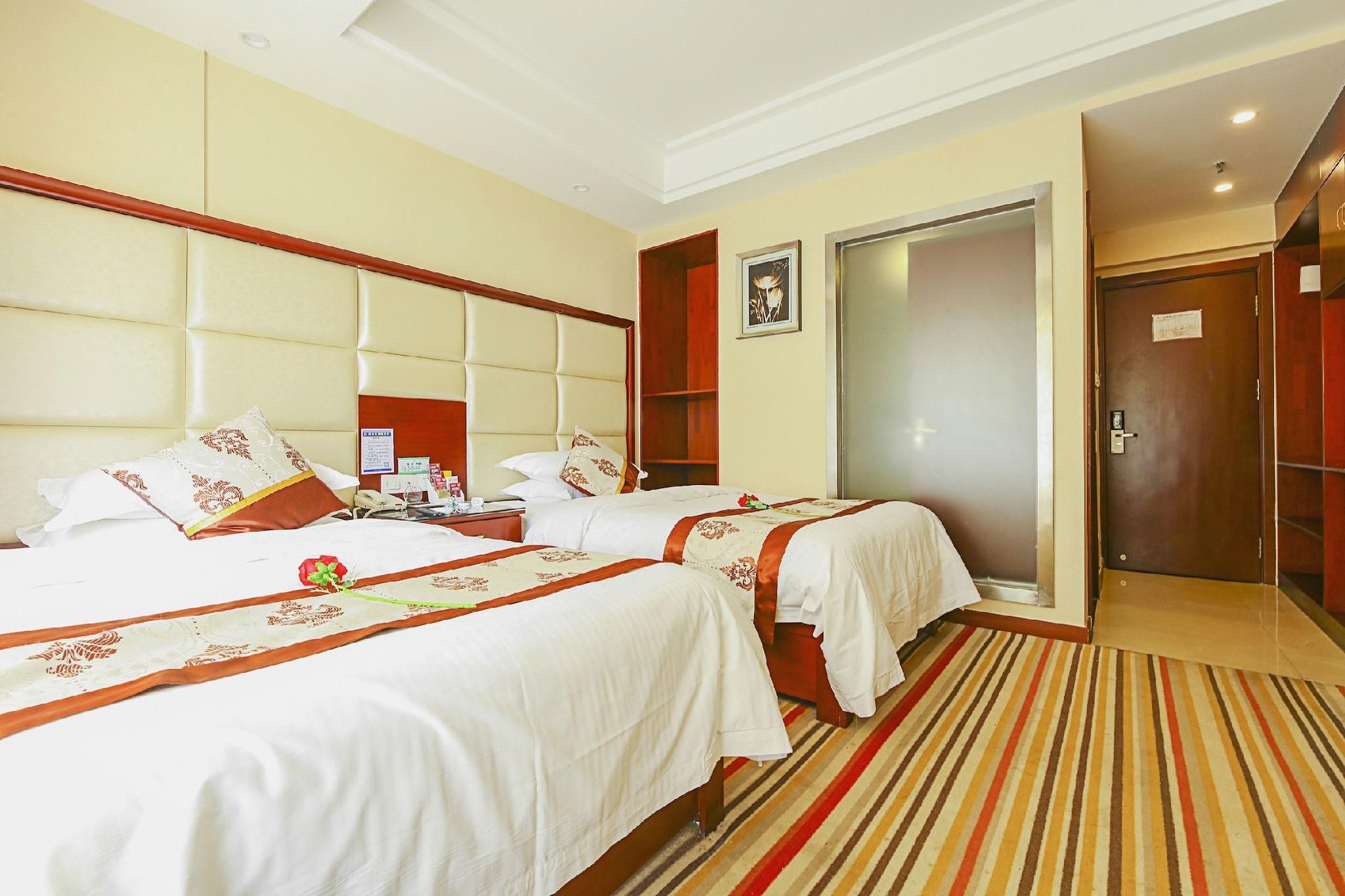A hotel room with two beds, a large padded headboard, a wooden wardrobe, a door, and a striped carpet.