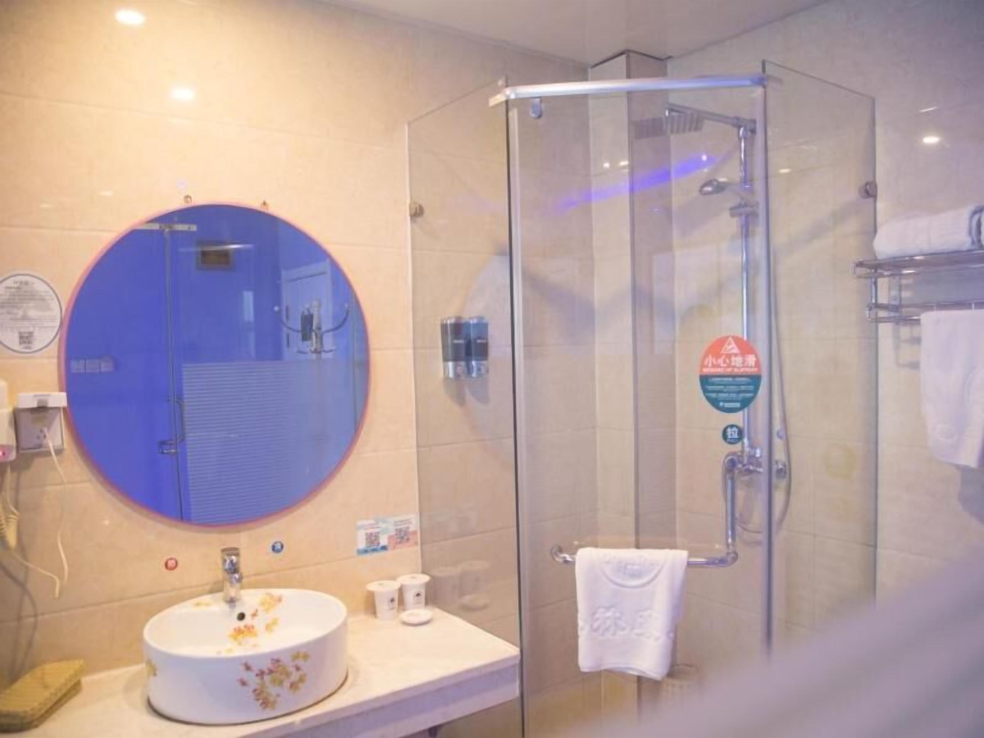 A bathroom with a round mirror, a sink with floral design, a glass shower enclosure, and a towel rack.