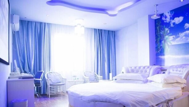 Una camera d'albergo moderna con un letto rotondo, una scrivania con sedia e un'ampia finestra con tende.