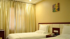 Une chambre d’hôtel avec deux lits, une table de chevet avec une lampe, un tableau au mur et une fenêtre avec des rideaux.