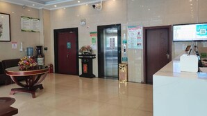 Un'area della reception di un hotel, con una scrivania, un distributore di acqua, un estintore, un orologio e un ascensore.