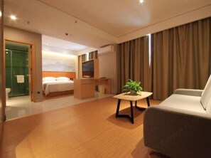 Une chambre d’hôtel avec un lit, un bureau, une télévision, un canap é et une plante.