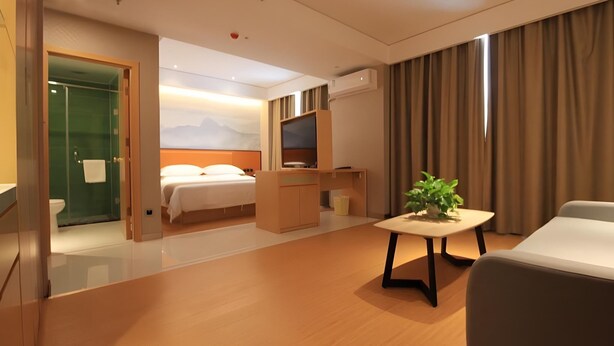 A hotel room with a bed, a desk, a TV, a plant, and a shower area. - Greentree Inn Zhengzhou Gongyi Xinxing Road (Zhengzhou)