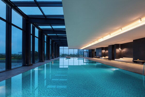 Une piscine intérieure dotée d’un toit en verre, de grandes fenêtres et d’un design moderne.