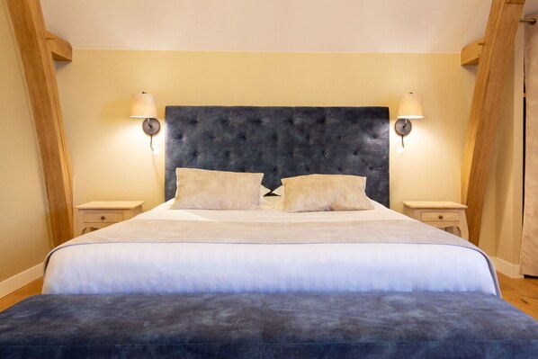 Une chambre à coucher avec une tête de lit capitonnée, deux tables de chevet et deux lampes fixées au mur.