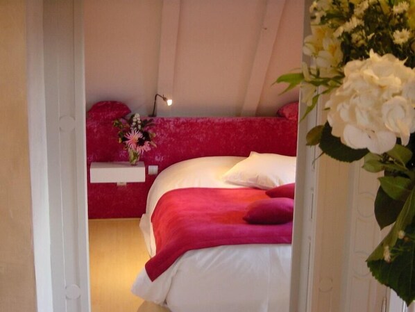 Un dormitorio con cama, mesita de noche y un jarrón con flores.