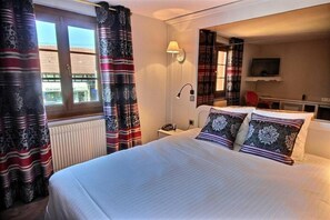 A hotel room with a large bed, a bedside lamp, a TV, and a view of the outside.