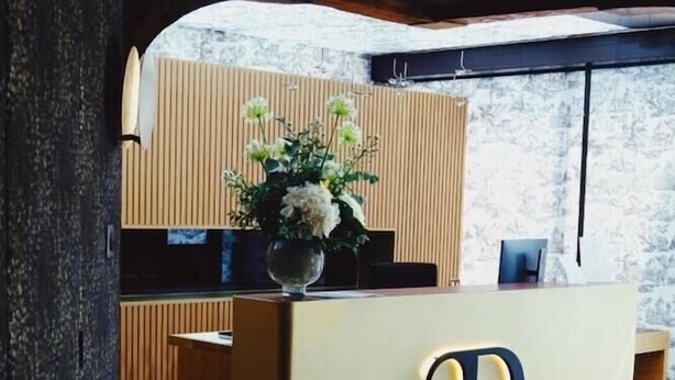 A reception desk with a large illuminated 'R' sign, a vase with flowers, and a wooden panel wall in the background. - Hotel Restaurant Le Relais de la Poste (La Wantzenau)