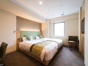 A hotel room with a double bed, a small desk, a chair, a window, and a wall-mounted TV.