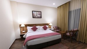 Ein Hotelzimmer mit einem großen Bett, zwei Nachttischen, einem Sessel, einem kleinen Tisch, einem Teppich und einem Gemälde vom Eiffelturm.