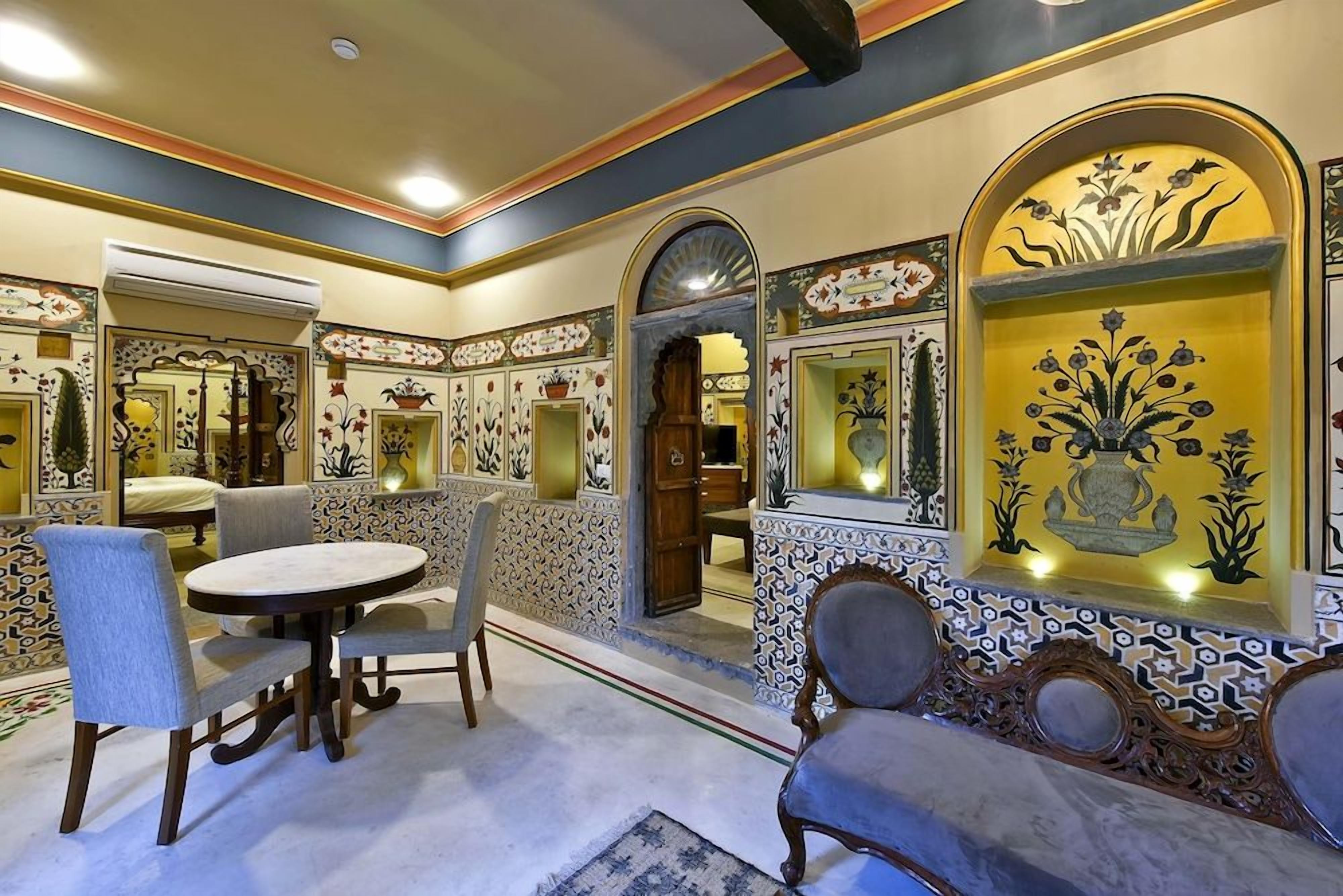 A dining area with a round table and chairs, ornate wall decorations, and a patterned floor.