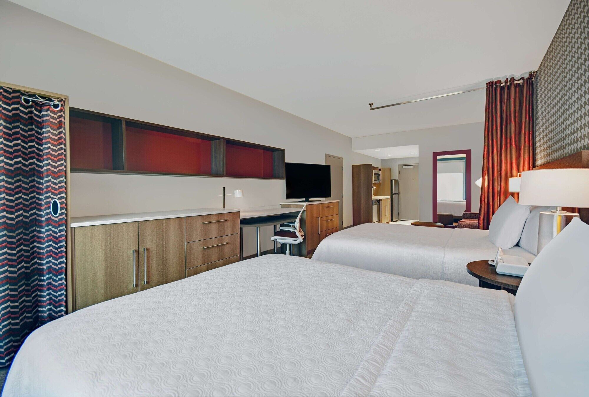 Una habitación de hotel con dos camas, un escritorio, un televisor y un baño con cortina de ducha.