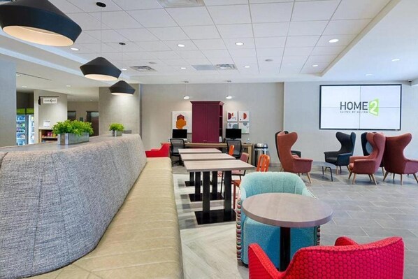 A modern hotel lobby with a seating area, a reception desk, and a large screen displaying "HOME2". - Home2 Suites by Hilton Blacksburg (Blacksburg)
