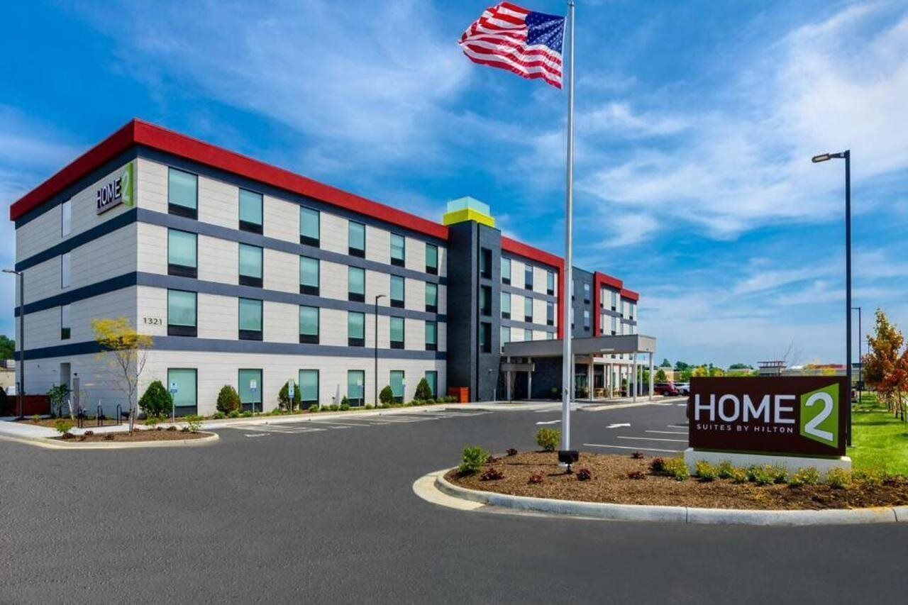 Un moderno edificio de hotel con fachada roja y blanca, un asta con la bandera estadounidense y un letrero que indica que es un hotel Hilton.