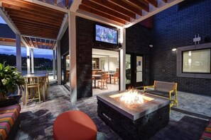 Un espace extérieur aménagé en terrasse, avec un foyer, des sièges et un écran de télévision fixé au mur.