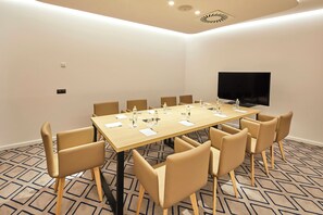 Une salle de conférence avec une longue table, huit chaises, un téléviseur à écran plat et des bouteilles d’eau posées sur la table.