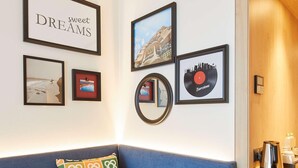 A blue sofa with colorful cushions, a framed picture of a cityscape, a framed picture with the text "sweet DREAMS", and a framed vinyl record. - Hampton By Hilton Barcelona Fira Gran Via (L'Hospitalet de Llobregat)