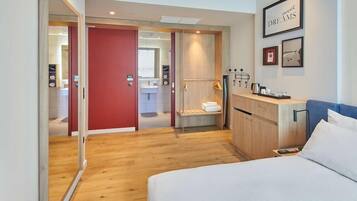 A hotel room with a bed, a wooden wardrobe, a red door leading to a bathroom, and a wall with framed pictures.