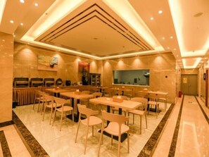 A spacious dining area with multiple tables and chairs, a kitchen area with appliances, and a tiled floor.