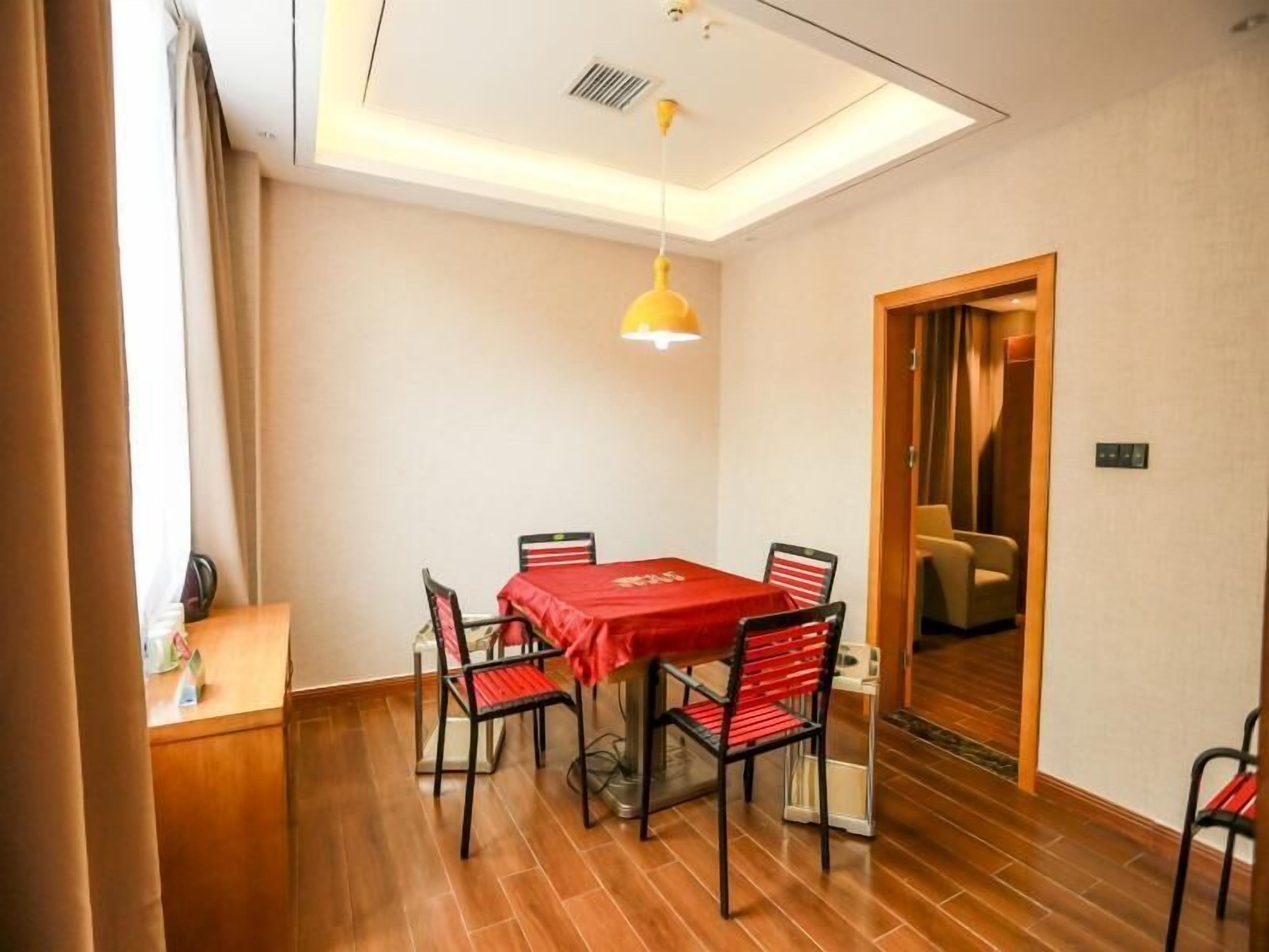 A dining area with a red table and black chairs, a yellow pendant light, and a wooden floor.