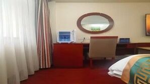 A hotel room with a desk, chair, bed, and a round mirror on the wall. - Greentree Inn Beijing Fengtai Dacheng Road Huanleshuimofang Business Hotel (Beijing)