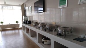 Un'area buffet con diverse postazioni di servizio, una televisione a schermo piatto montata a parete e una panca decorata con piante in vaso.