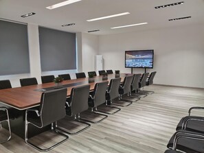 Une salle de conférence avec une longue table, des chaises noires, un téléviseur à écran plat fixé au mur et un écran de projection.