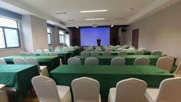 Un salón de conferencias con varias mesas y sillas, una pantalla de proyector y un atril.