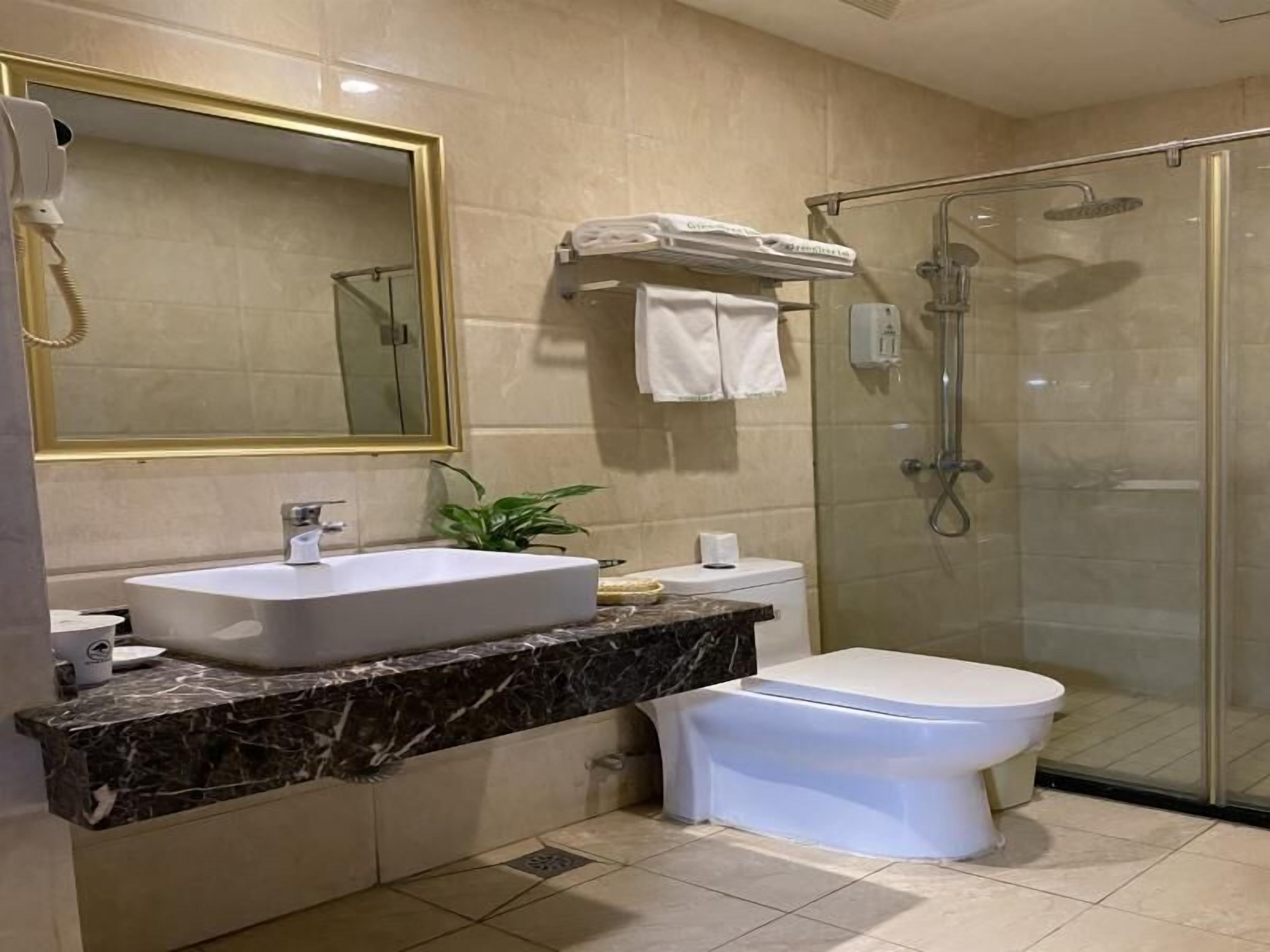 A modern bathroom with a large mirror, a sink, a toilet, and a glass-enclosed shower.