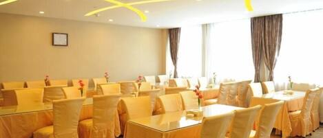A conference room with round tables and chairs, a framed picture on the wall, and curtains on the windows.