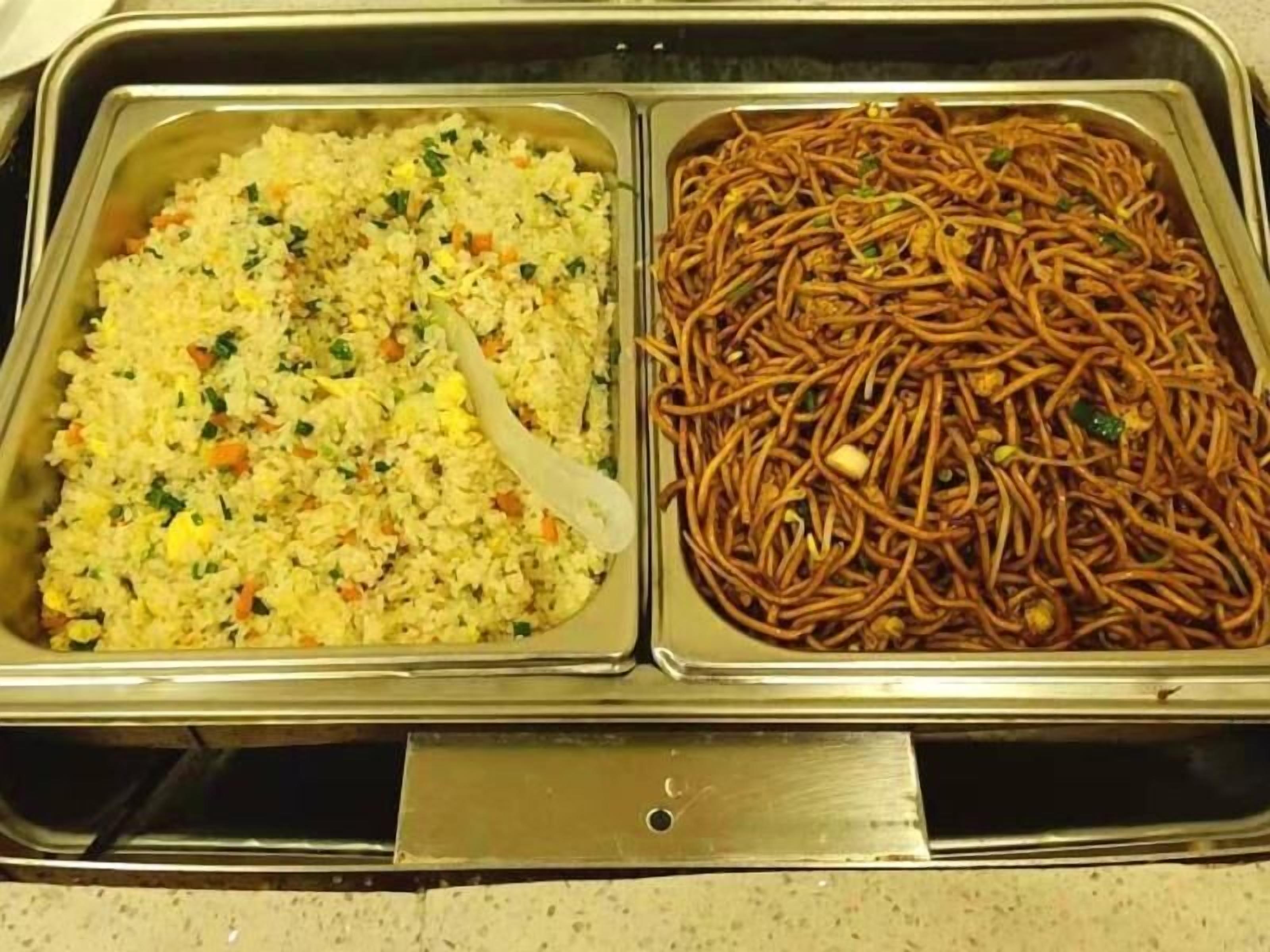 A stainless steel buffet tray with two sections: one containing fried rice with vegetables and another with stir-fried noodles.