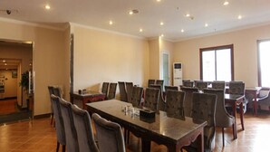 A conference room with a long table and multiple chairs, equipped with ceiling lights and an air conditioning unit.