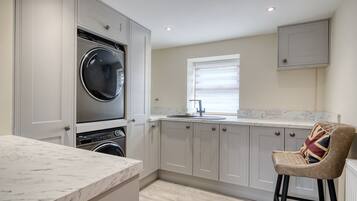 A modern kitchen with built-in appliances, a marble countertop, and a window with blinds.