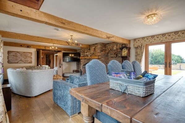 A cozy living room with a wooden ceiling, a fireplace, and a dining area with a wooden table and blue patterned chairs. - The Residence - Sleeps 10, 2 Hot Tubs near Durham & Bishop Auckland (Oakenshaw)