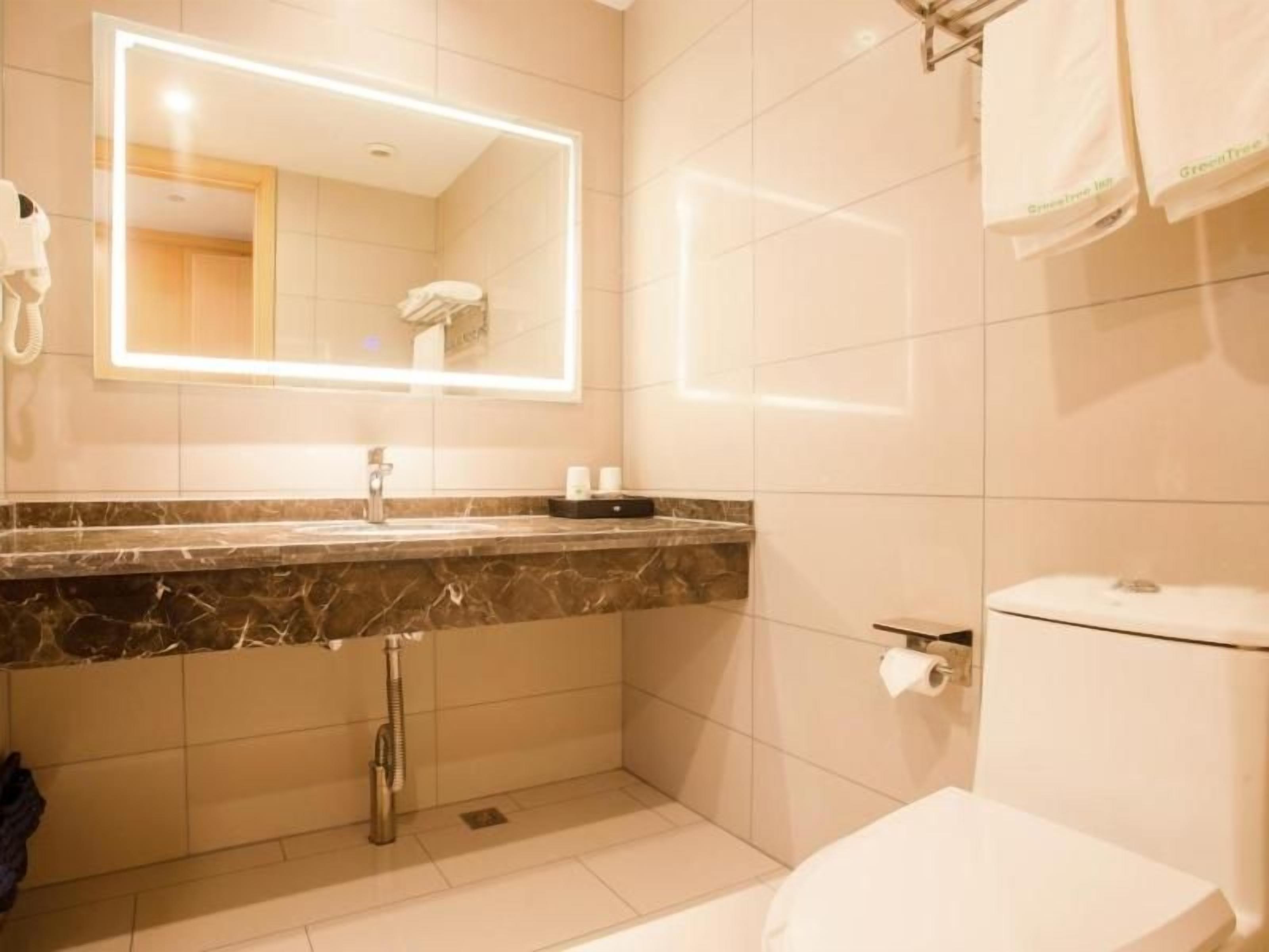 Une salle de bain avec un lavabo en marbre, des toilettes et un miroir doté d’un éclairage intégré.