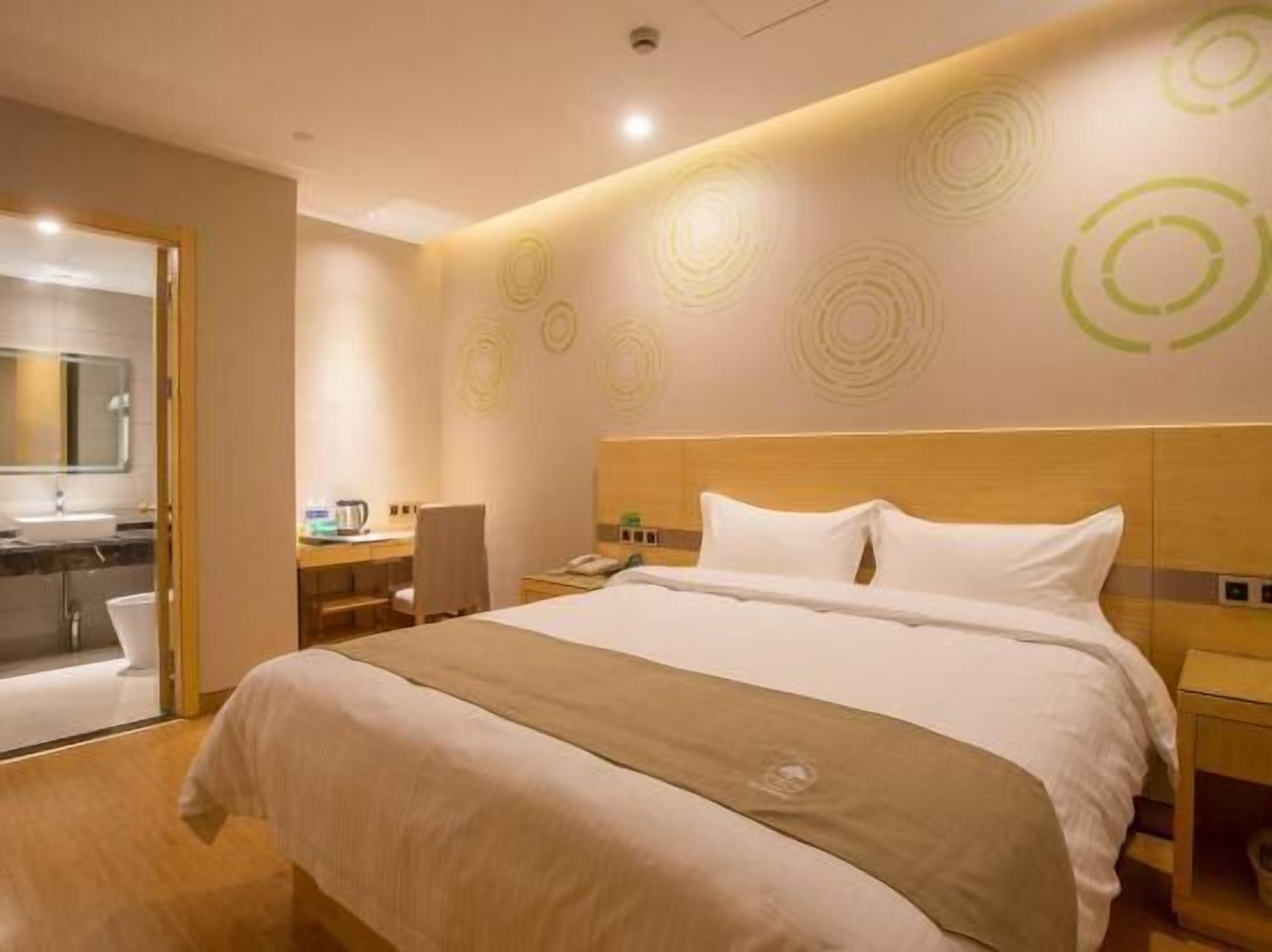 A hotel room with a large bed, a desk with a chair, a small table, and a mirror.
