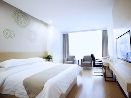 Quarto de hotel com uma cama grande, duas poltronas, uma escrivaninha com computador e uma janela ampla.