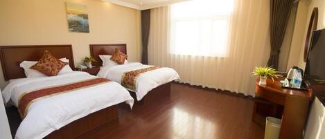 A hotel room with two beds, a TV, a desk with a plant, and a window with curtains.
