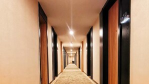 A long, narrow hotel corridor with a patterned carpet, wooden doors, and a neutral color scheme. - Green Tree Inn Huangshan Yi County Xidi Hongcun (Huangshan)